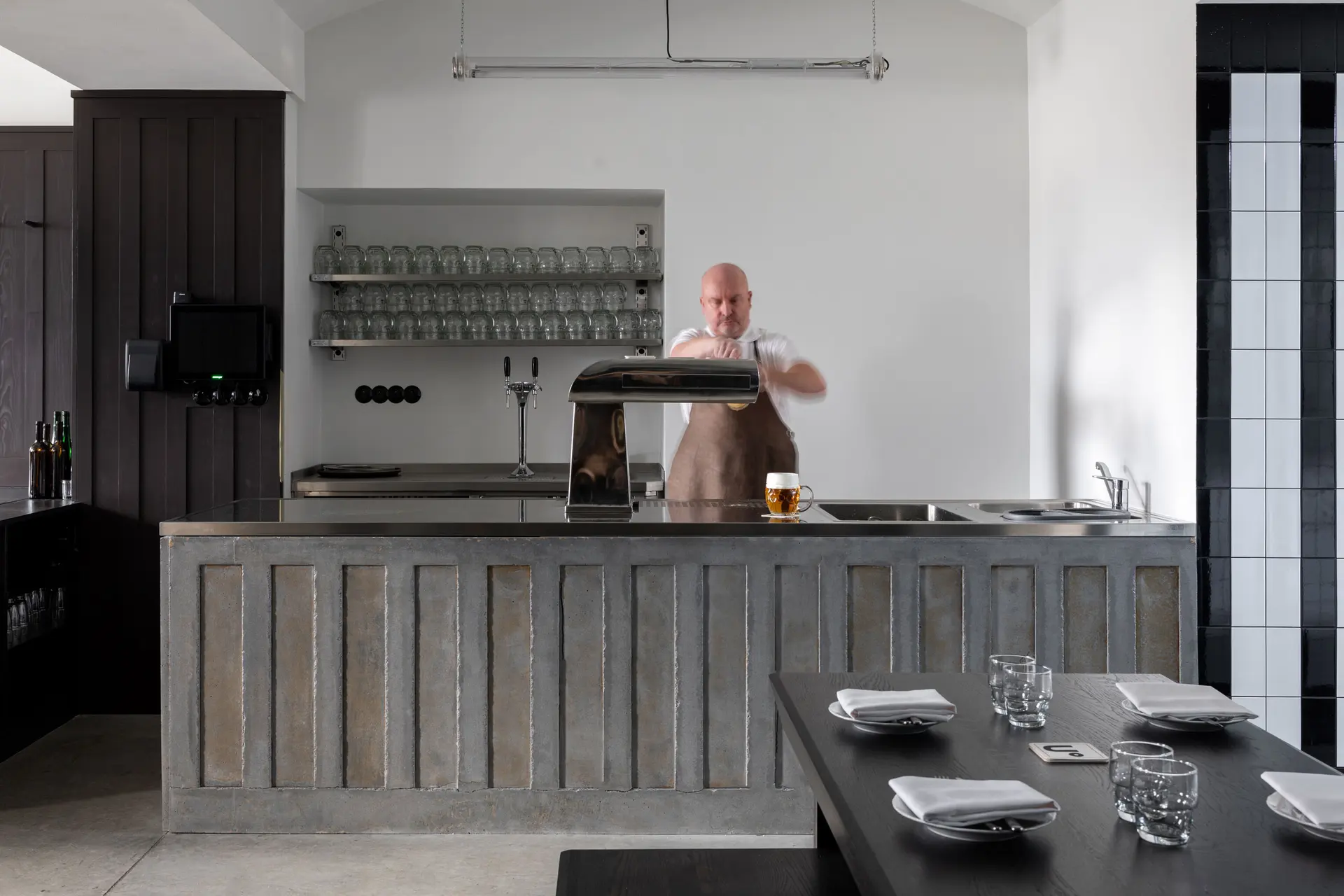 Bartender pouring beer behind a minimalist restaurant bar.